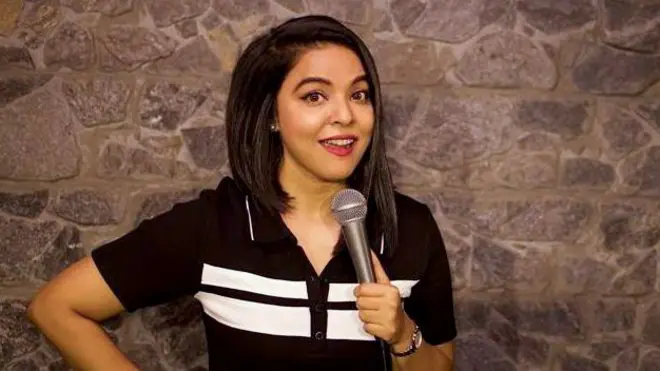 Ankita Shrivastav, wearing a black-and-white T-shirt, is standing on a stage and holding a mic in her hand.
