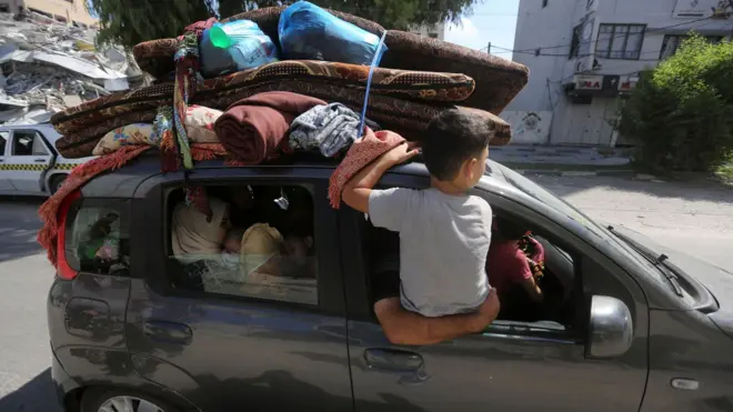 A boy sits in the open window of a heavily laden car