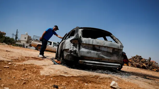 فلسطيني يتفقد سيارة محترقة بعد هجوم شنه مستوطنون على قرية كفر مالك في الضفة الغربية المحتلة