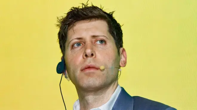 Sam Altman, con auriculares y micrófono a un lado de la boca, sobre fondo amarillo