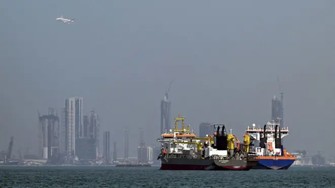 Denizin üzerinde yan yana duran iki ticari gemi. Arkada Dubai silüeti görünüyor.