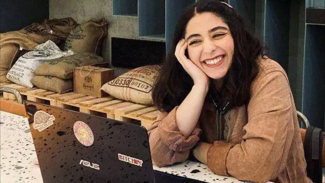 Parnia Abassi sonríe. Está sentada en una barra en una cafetería frente a su computadora