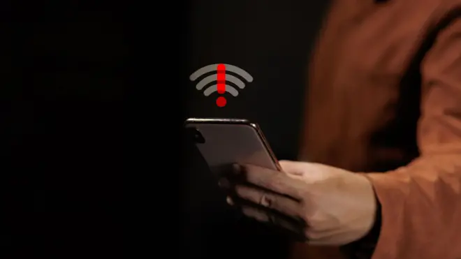 Hand holding mobile phone showing wireless signal problem with red exclamation mark. Concept of no internet connection, network error, system failure and offline status.