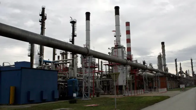 Нефтеперерабатывающий завод: много вертикальных труб и длинная труба, идущая над землей