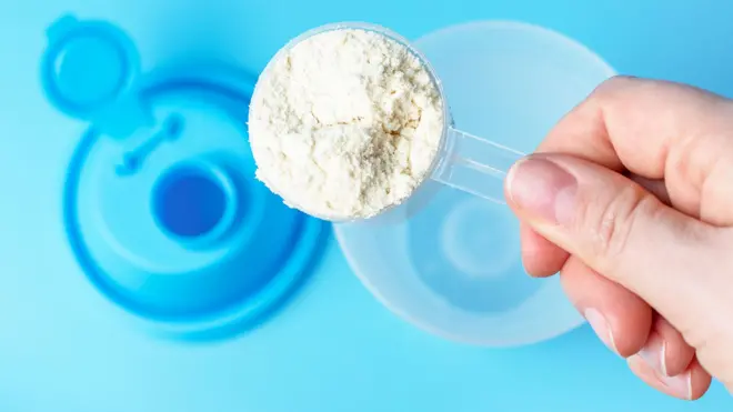 A person scooping white powder supplement into plastic cup