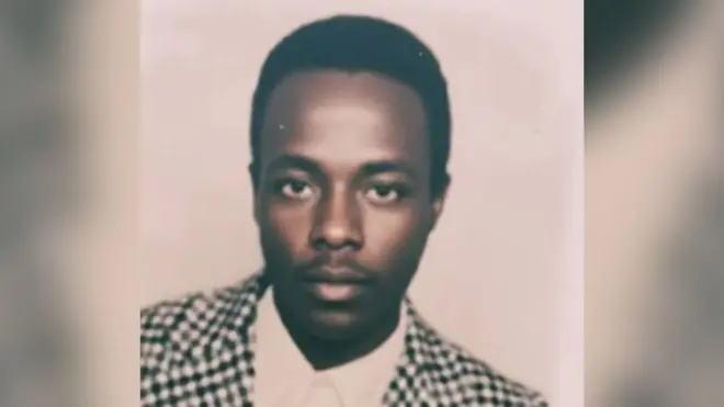 An old passport photo of Biniam Solomon, He is wearing a dog-tooth jacket and white shirt.