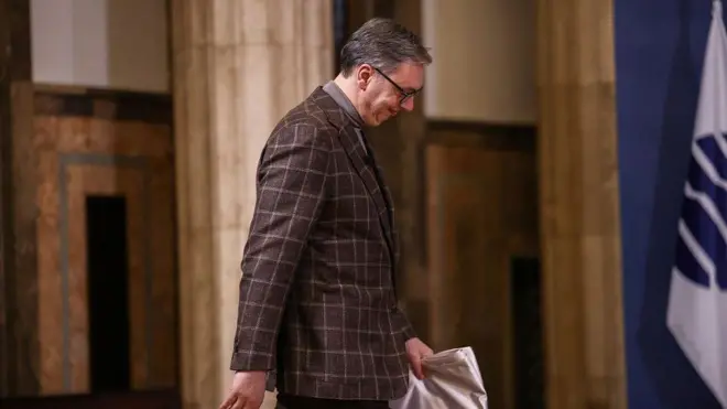 Predsednik Vučić u kariranom sakou i sivoj rolci, pognute glave, hoda