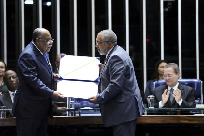 O ministro Benedito Gonçalves e o senador Paulo Paim no Plenário do Senado. Ambos são homens negros idososroleta de clubes de futebolterno. Paim estende um diploma comemorativo a Benedito