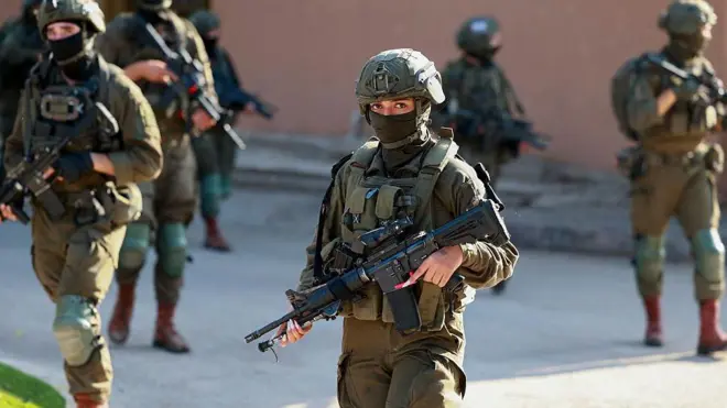 Militares israelíes caminan por una calle. En primer plano, lo que parece ser una mujer. 