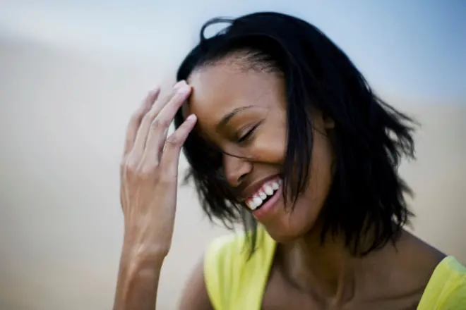 Black woman dey smile as she stand for sand dune