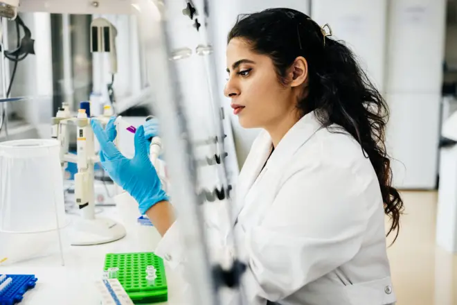 The scientist concentrates on inspecting a sample vial, highlighting the attention to detail essential for accurate experimental results. The laboratory setup underscores a professional and methodical approach.