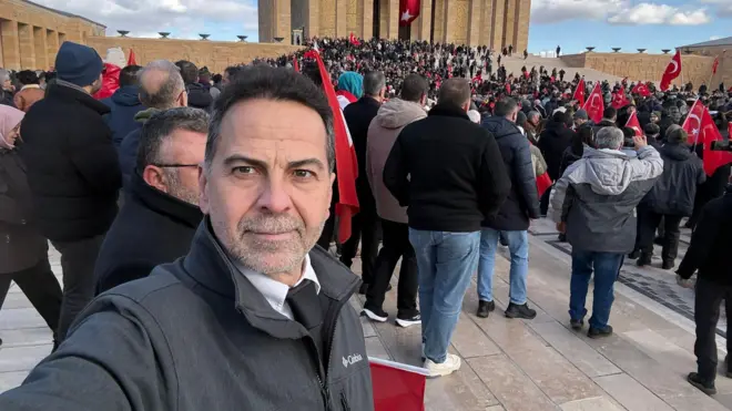 Nasuh Mahruki Anıtkabir'de toplanan kalabalığa arkası dönük selfie çekiyor. Kalabalık Türk bayrakları taşıyor.