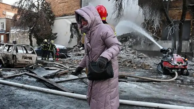 Ukrayna'nın Kiev kentinde, 12 Ocak 2026'da Rus insansız hava aracı saldırısının ardından yıkılan bir binada itfaiyeciler yangını söndürürken bir kadın yürüyor. 