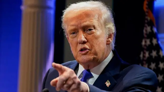 星条旗を背に、前を指さして話すトランプ氏