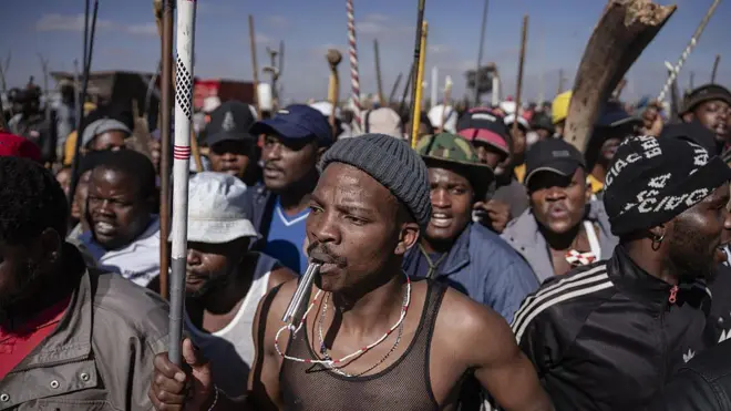 Man hold club odas hold stick for im back, during protest for South Africa