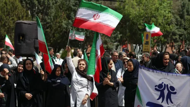 Медицинские работники, держащие иранские флаги, принимают участие в акции протеста против американо-израильских ударов по медицинским учреждениям у больницы имени имама Хомейни в Тегеране, Иран, 6 апреля 2026 года.