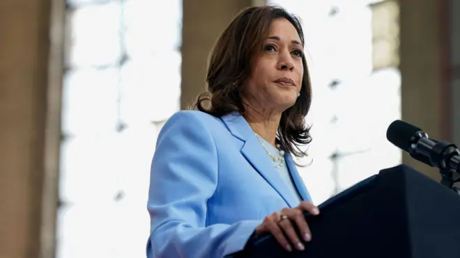 Kamala Harris porte un costume bleu et semble hors cadre alors qu'elle se tient devant un microphone.