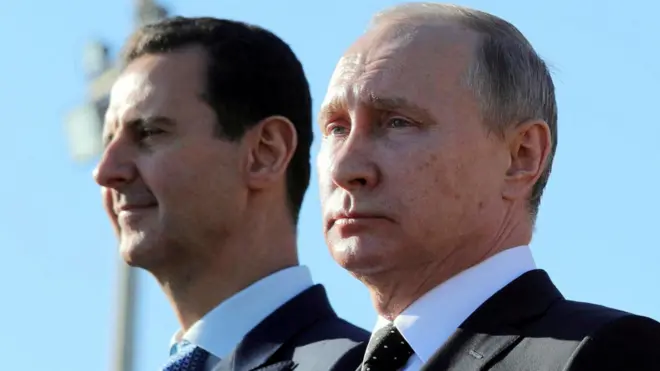 Ifoto yo mu bubiko igaragaza Perezida w'Uburusiya Vladimir Putin (iburyo) na Perezida wa Syria Bashar al-Assad begeranye, ubwo Putin yari yasuye ikigo cya gisirikare cy'ingabo zirwanira mu kirere z'Uburusiya cy'i Hmeymim, muri Syria, mu mwaka wa 2017