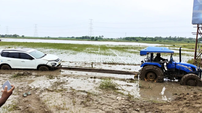 పొలాల్లో కూరుకుపోయిన కార్లను ట్రాక్టర్లతో బయటికి తీసుకొస్తున్నారు