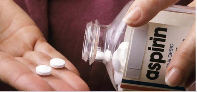 يد شخص تمسك زجاجة أسبرين صغيرة وتضع حبة منه في اليد الأخرى.