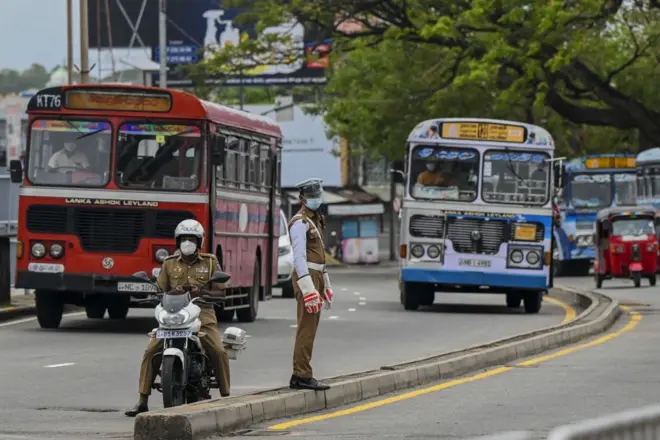A police officer stands on a road divider as he directs traffic in Colombo
