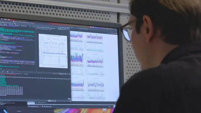 Чоловік перед монітором компʼютера, на якому зображені графіки