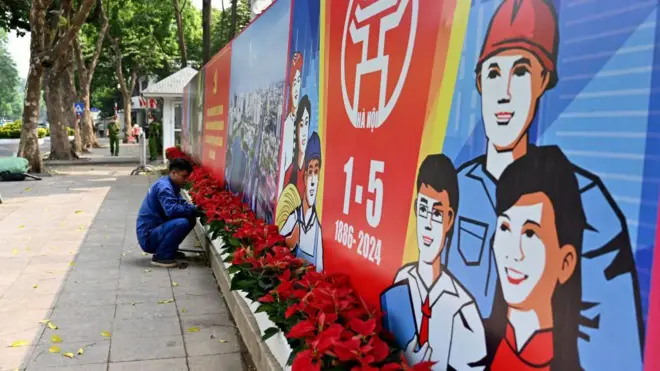 Aworan oṣiṣẹ to n gbin ododo niwaaju patako ikede ọjọ awọn oṣiṣẹ