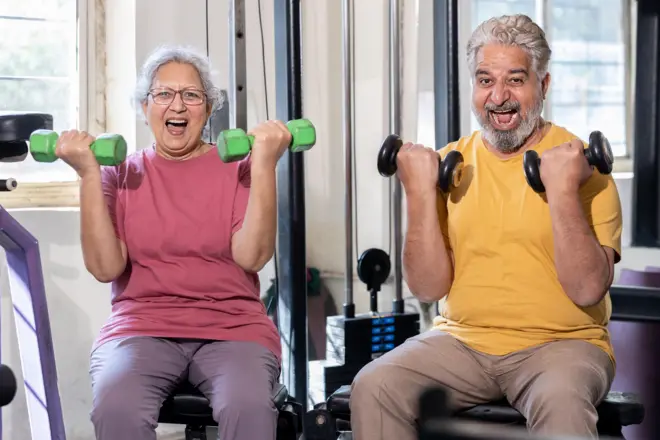 Happy indian senior couple have fun exercises in gym, Excited elderly people do weight lifting training with dumbbells at health club to stay fit. Retirement life. - stock photo