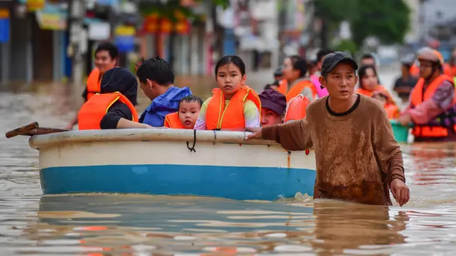 Мужчина ведет лодку с детьми по затопленной улице во Вьетнаме 20 ноября 2025 года