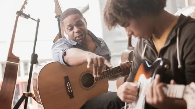 Um homem ensinando um adolescente a tocar violão/guitarra