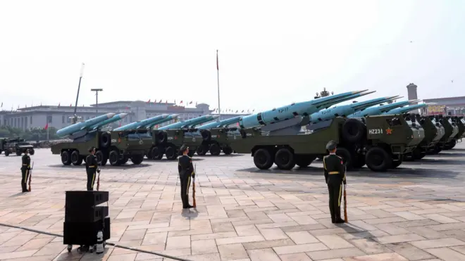 Chinese missiles parade through Tiananmen Square while soldiers in green military clothing watch on.
