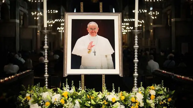 İngiltere'nin başkenti Londra'daki Westminster Katedrali'nde  Papa Francesco'nun ölümü, fotoğrafının etrafına konulan sarı çiçeklerle anılıyor.