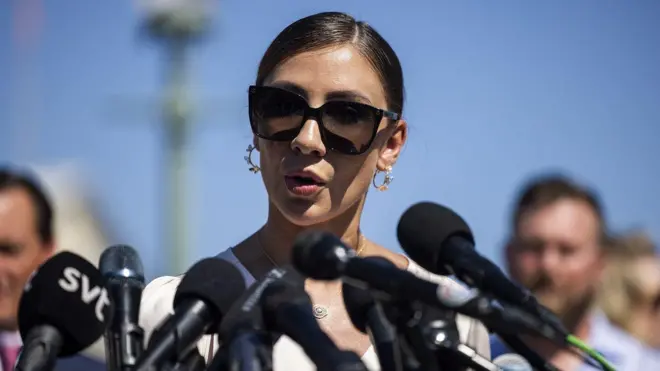 Mulher falando ao ar livre, cercada por microfones e pessoas