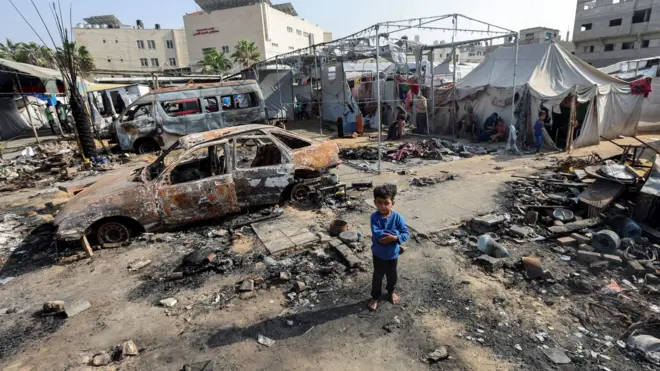 طفل يظهر في واجهة صورة تظهر خيام نازحين في غزة وسط الدمار