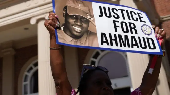 A demonstrator holds a sign at the Glynn County Courthouse as jury selection begins in the trial of the shooting death of Ahmaud Arbery