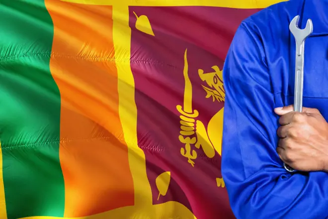 Sri Lankan Mechanic in blue uniform is holding wrench against waving Sri Lanka flag background