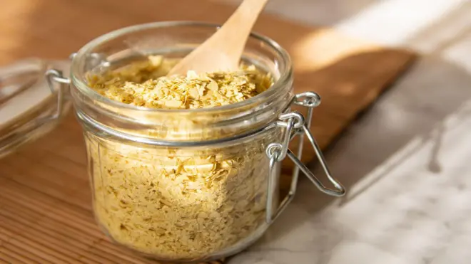 نمای نزدیک از مخمر غذایی در یک شیشه شیشه ای با قاشق چوبی. 
