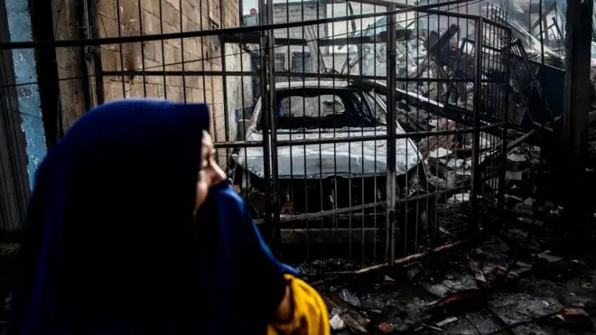 Seorang perempuan melintas di depan bangkai mobil dan rumah akibat kebakaran Depo Pertamina di Plumpang, Jakarta.