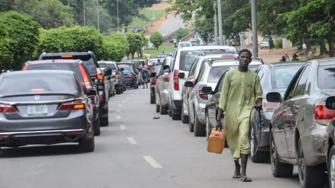 Cars on queue wit man holding keg of petrol and hose