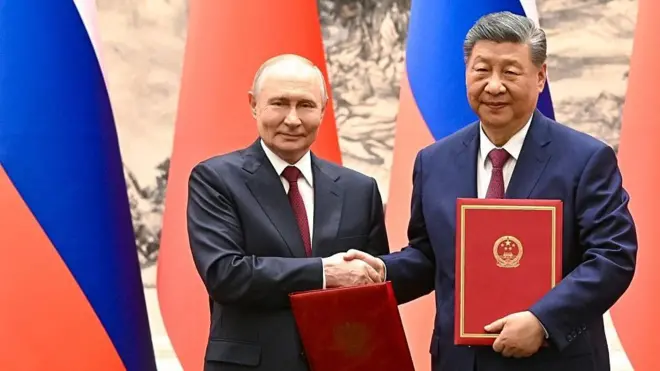 Putin ve Şi imzaladıkları anlaşmaları ellerinde tutuyor ve tokalaşıyorlar
