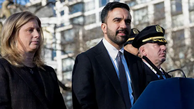 Джессика Тиш и Зохран Мамдани (у микрофона) стоят на улице, рядом двое мужчин в форме.