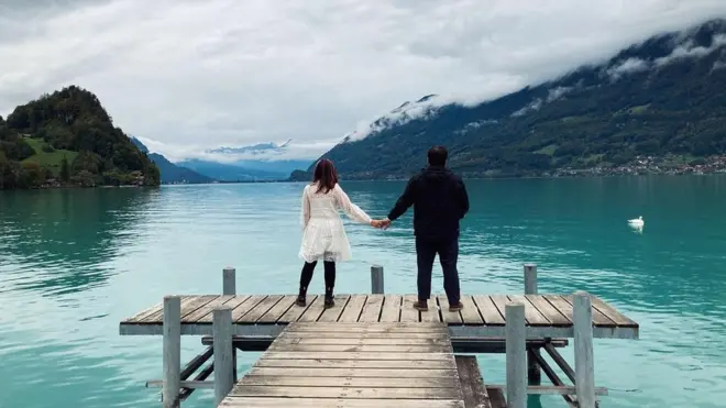 A couple stand, holding hands on the landing pier in Iseltwald