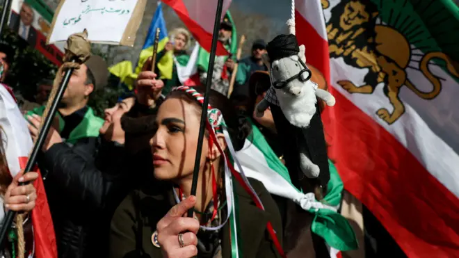 Genç bir kadın bayrak sallıyor. Arkada İran'ın monarli döneminde kullanılan bayrağı var. 