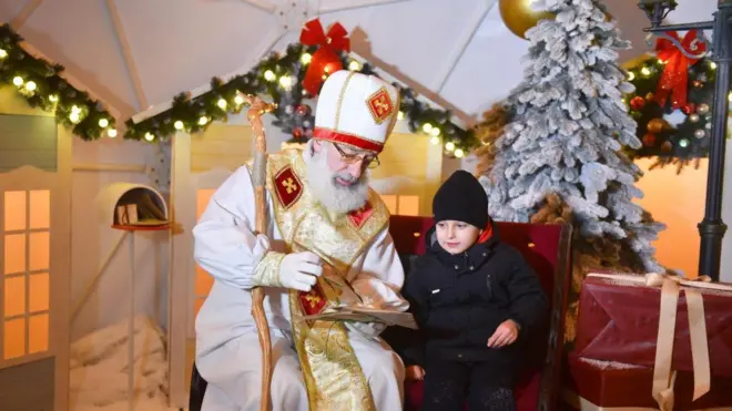 Чоловік у костюмі Святого Миколая спілкується із хлопчиком. Резиденція Миколая у новорічних прикрасах.