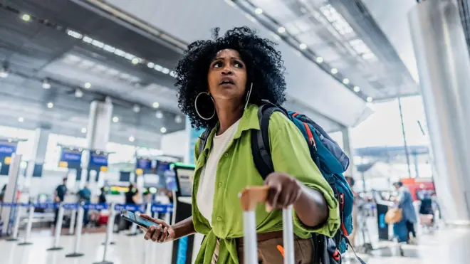 የተጨነቀች ሴት በአውሮፕላን ማረፍያ ውስጥ ሻንጣዋን ይዛ