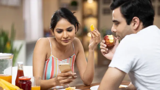 Couple eating food looking at phone.