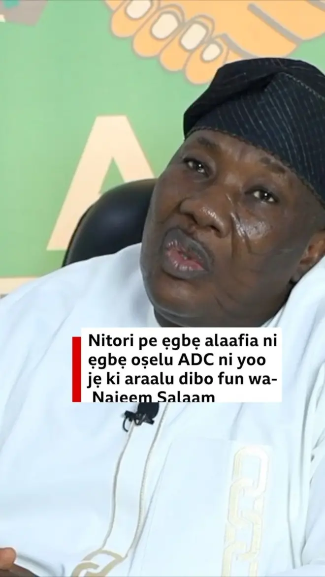 Najeem Salaam wọ aṣọ funfun, o jokoo lori aga 