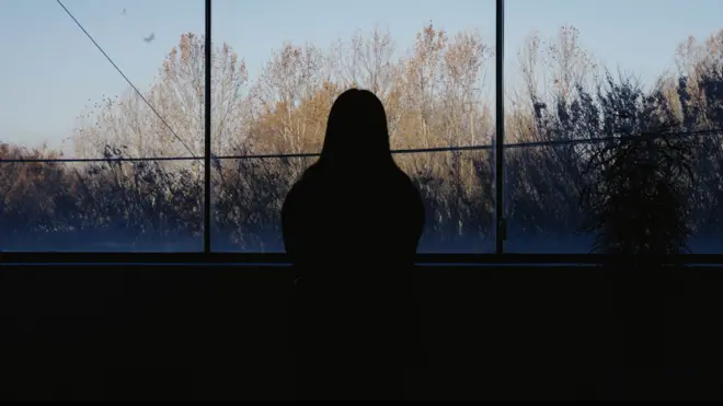一名女子凝視窗外的剪影，背景為樹木與綠意。