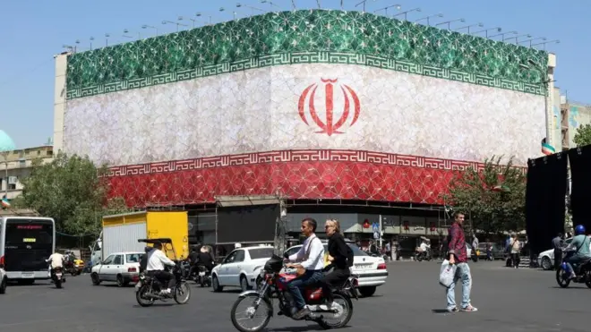 エンケラブ広場に臨む建物の二つの壁面にイラン国旗が大きく掲示されている。その前を車両や歩行者が行きかう