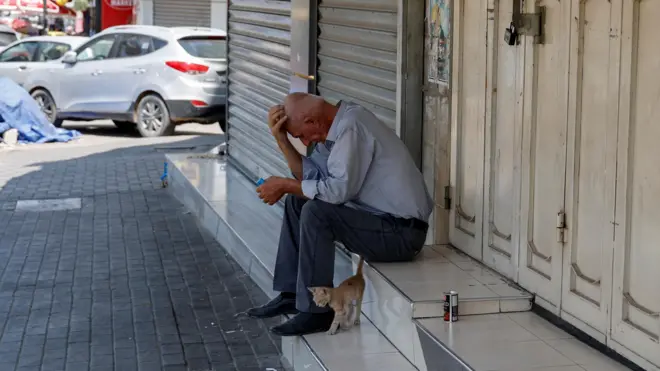 رجل يجلس خارج متجر مغلق خلال إضراب عام بعد مقتل ثلاثة مسلحين فلسطينيين في غارة بطائرة مسيرة إسرائيلية في جنين